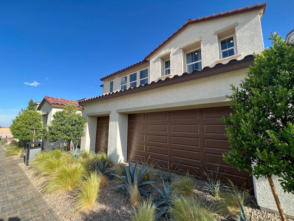 Desert-landscaped home exterior featuring a stone paver walkway, drought-tolerant agave plants, and stucco walls under a clear blue sky.